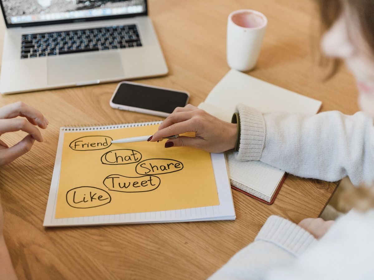 Two people sketching a plan in a notebook beside a laptop on a wooden table