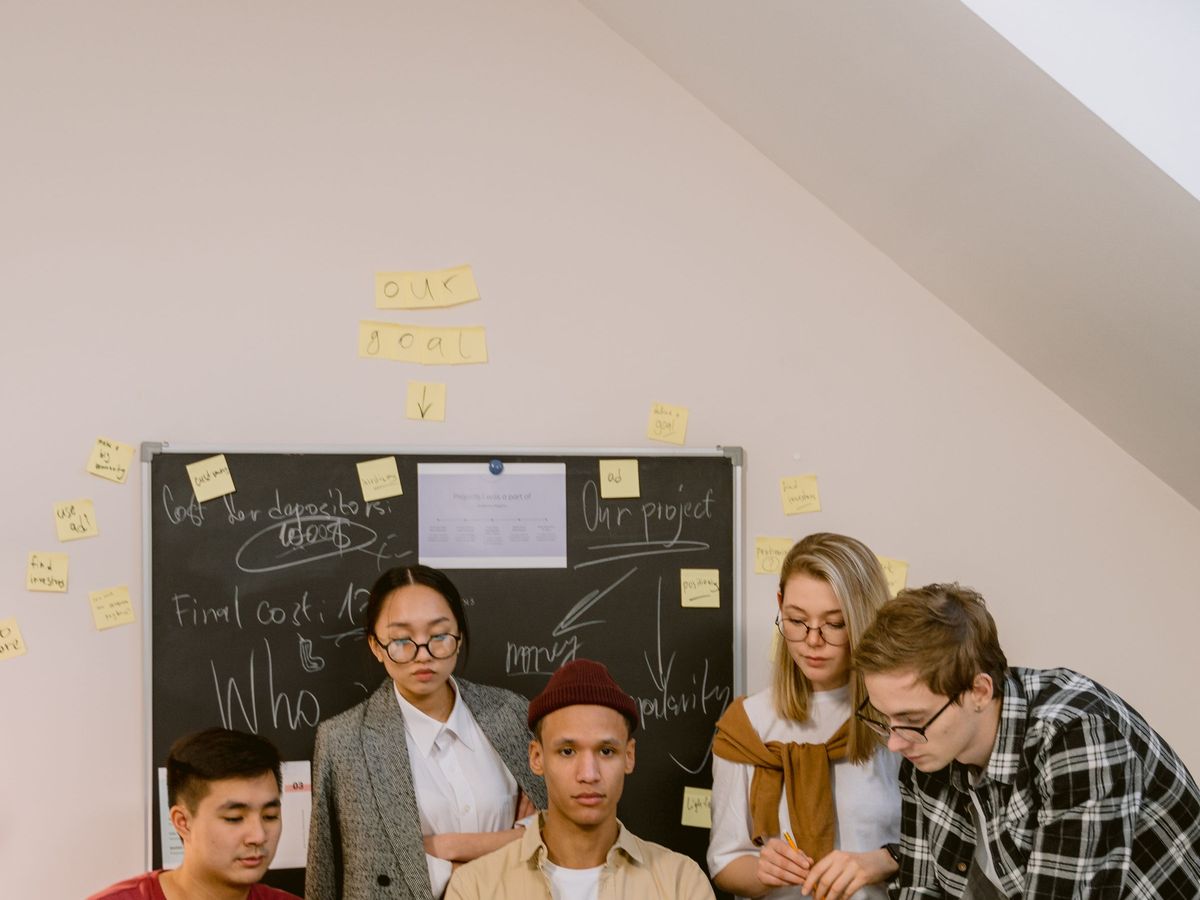 A small team gathered around a table with laptops, planning ideas on a board behind them